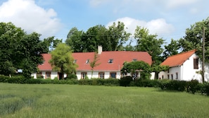 Un bâtiment blanc avec un toit rouge, entouré de verdure et d’arbres.