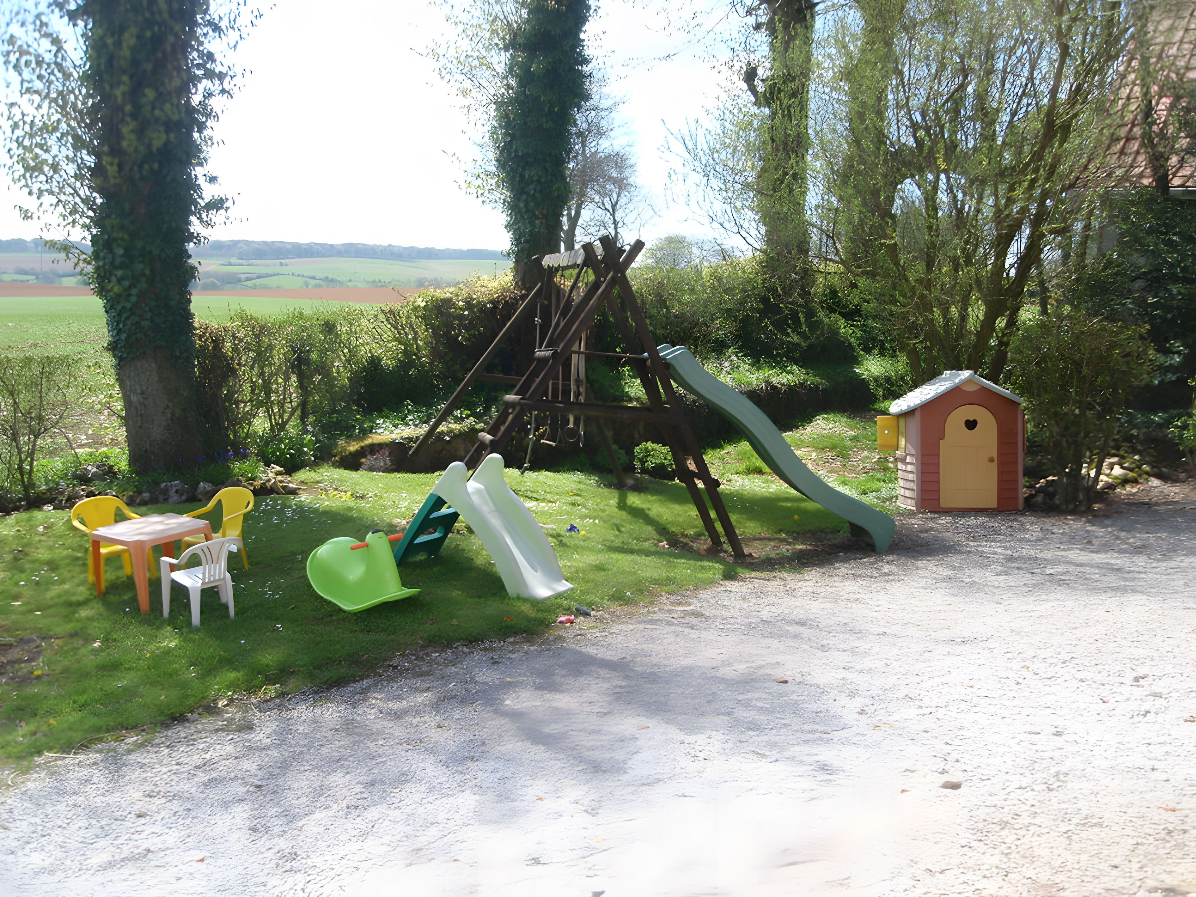 Une aire de jeux avec un toboggan, une structure d’escalade et une petite maison de jeu.