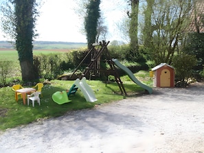 Une aire de jeux avec un toboggan, une structure d’escalade et une petite maison de jeu.