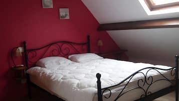 Un lit dans une chambre avec un plafond en pente et un puits de lumière, agrémenté d’un mur rouge et d’un cadre en métal noir.