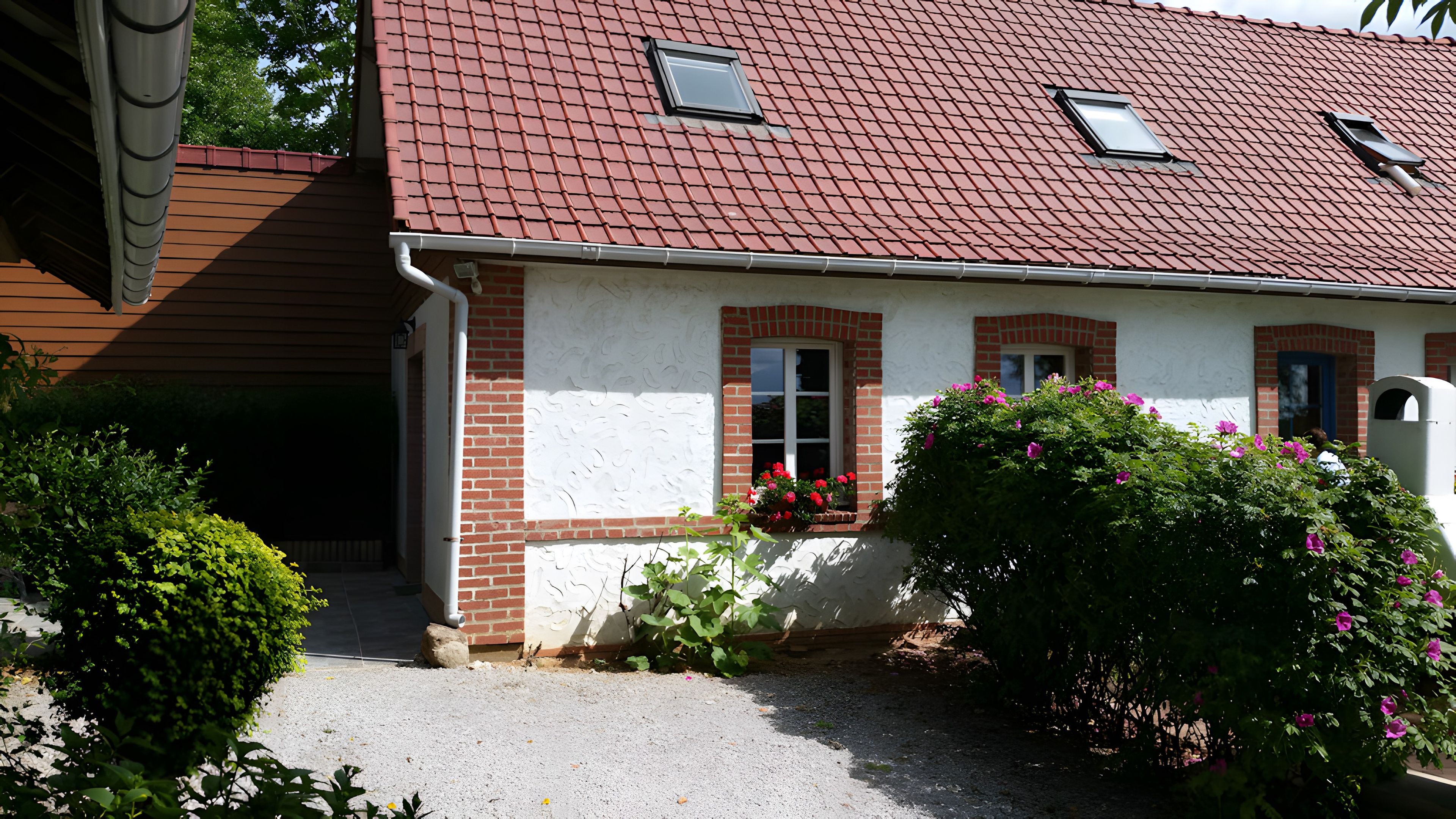 Une maison avec un toit recouvert de tuiles rouges, des murs en briques et une petite fenêtre.