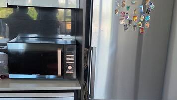 A compact kitchen with a stainless steel refrigerator, a microwave, and a red chair.
