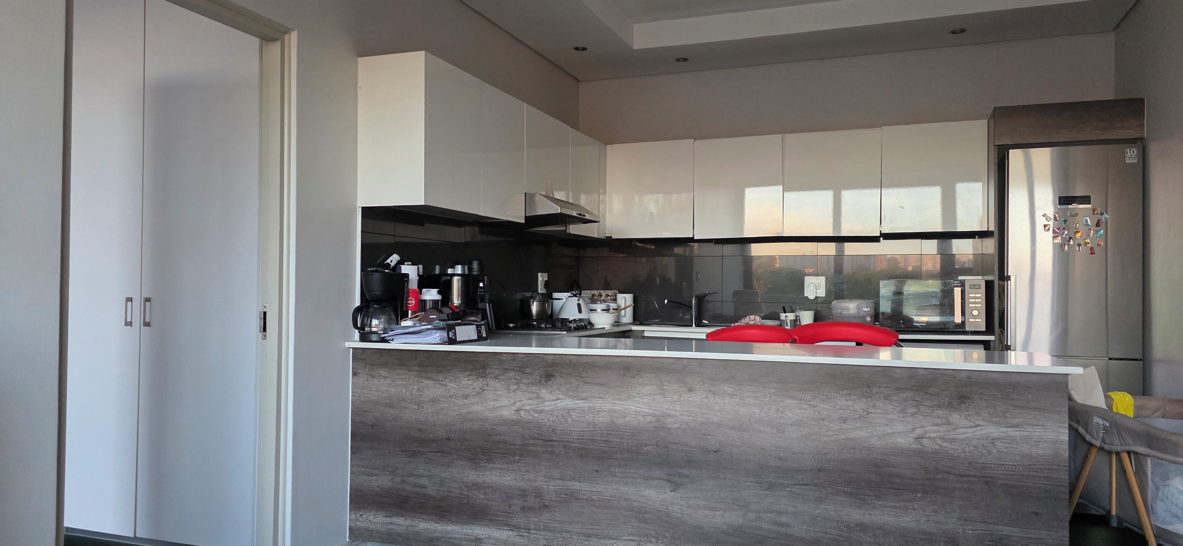 A modern kitchen with white cabinets, a stainless steel refrigerator, and a red chair.