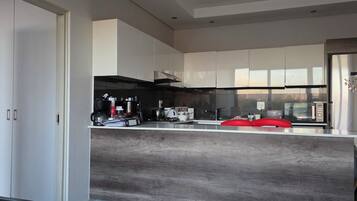A modern kitchen with white cabinets, a stainless steel refrigerator, and a red chair.