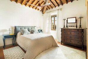 A bedroom with a bed, a dresser, a nightstand, a ceiling fan, and a window with curtains. - Villa Mare, Bolgheri by Geco Vacation Rentals (Bolgheri)