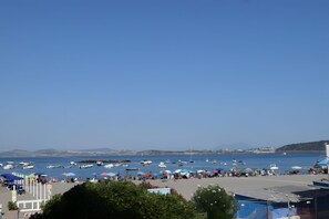 Eine Küstenlandschaft mit Booten, Sonnenschirmen und Menschen am Strand.