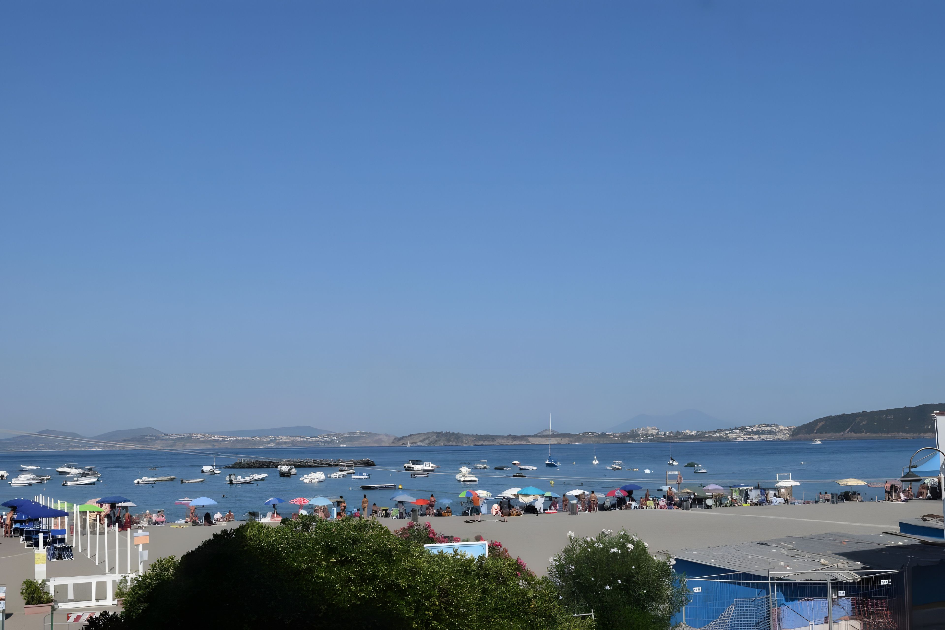 Eine Küstenlandschaft mit Booten, Sonnenschirmen und Menschen am Strand.