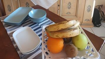A dining table with a white tablecloth, blue and white plates, a basket of bread, and fruits.