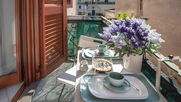 Ein Balkon mit einem Tisch für zwei Personen, einem Blumentopf und Blick auf Gebäude im Hintergrund.