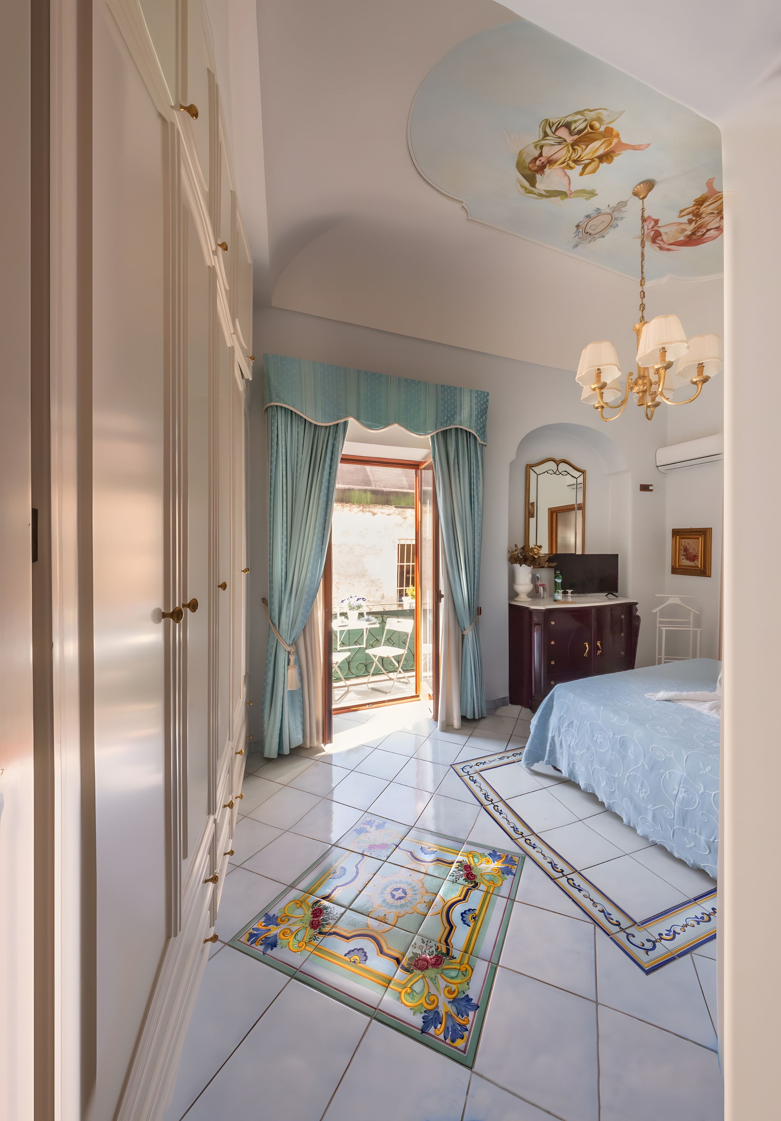 A bedroom with a bed, a dresser, a mirror, and a chandelier.