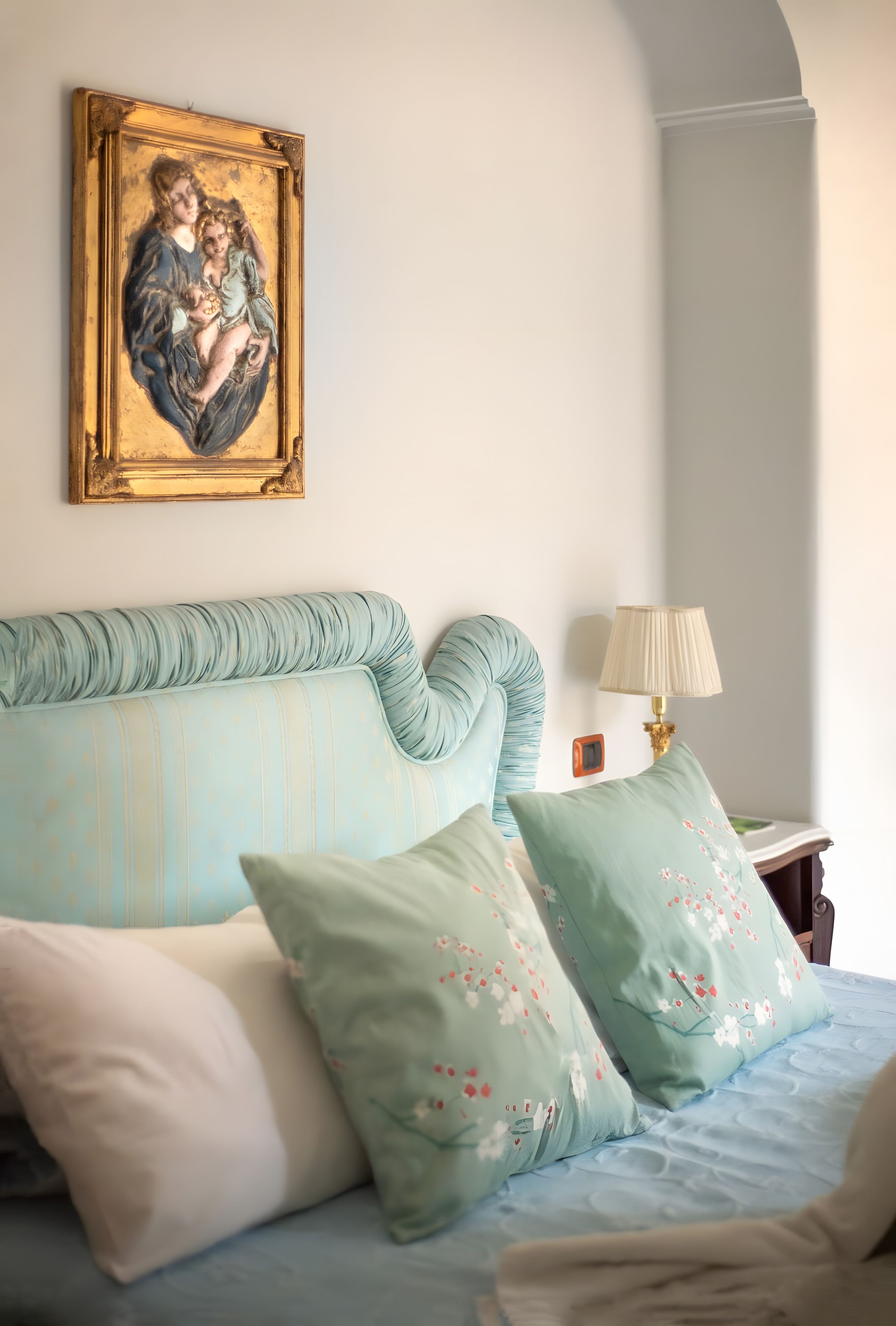 Ein Schlafzimmer mit einem Bett, Kissen, einem Nachttisch, einer Lampe und einem gerahmten Bild an der Wand.
