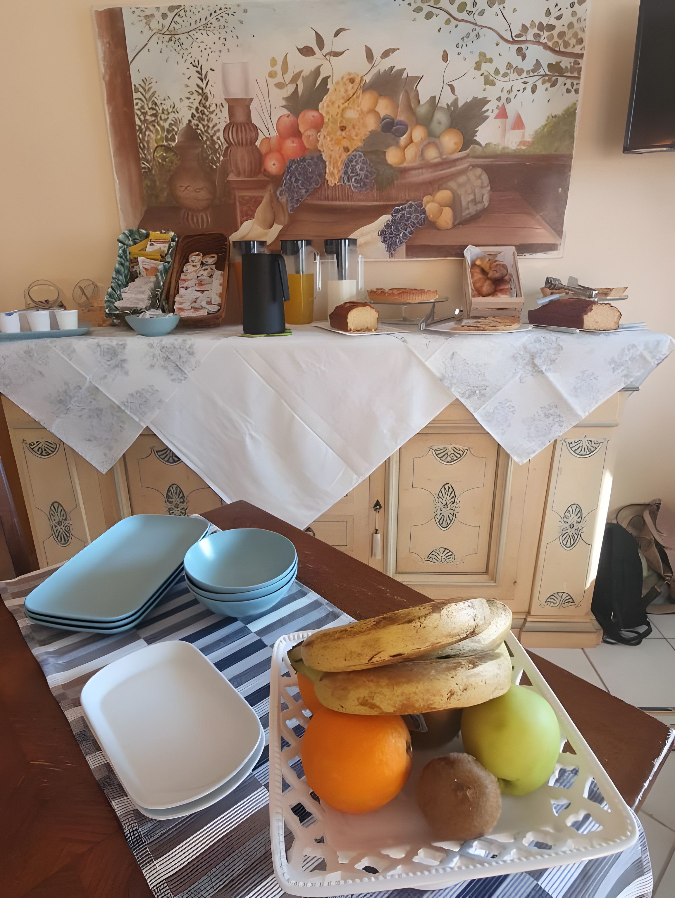 Ein Esstisch mit weißer Tischdecke, blau-weißen Tellern, einem Brotkorb und Früchten.