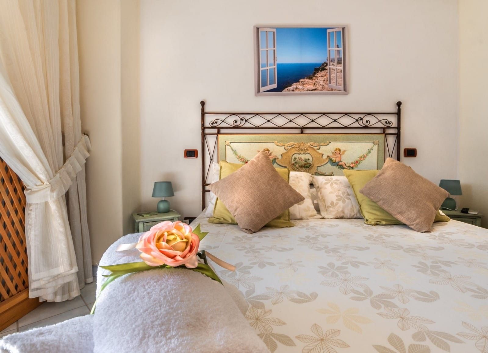 Un dormitorio con cama, cabecera decorativa, pintura de una escena costera y una ventana.