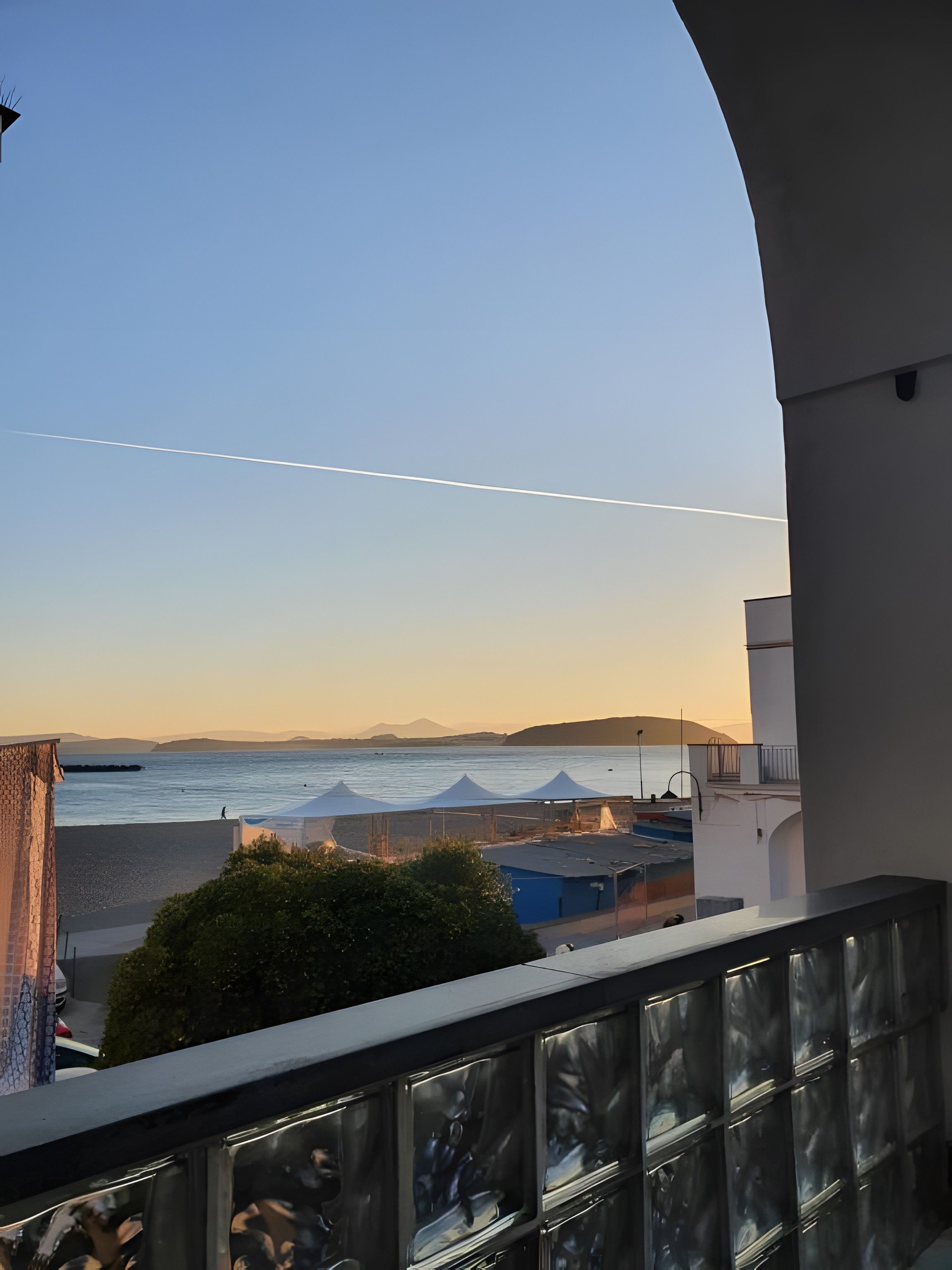A balcony with a view of the sea, a clear sky, and distant mountains.
