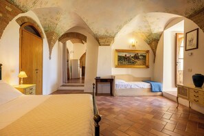 Quarto com cama, mesa de cabeceira, cômoda, pintura e porta que dá para outro aposento.