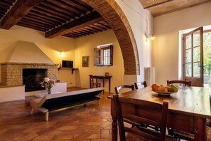 Uma sala de jantar com lareira de pedra, vigas de madeira e uma mesa posta para quatro pessoas.
