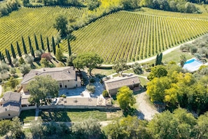 A vineyard with rows of grapevines, a stone building with a tiled roof, and a swimming pool. - Croce di Bibbiano, San Gimignano View (Bibbiano)