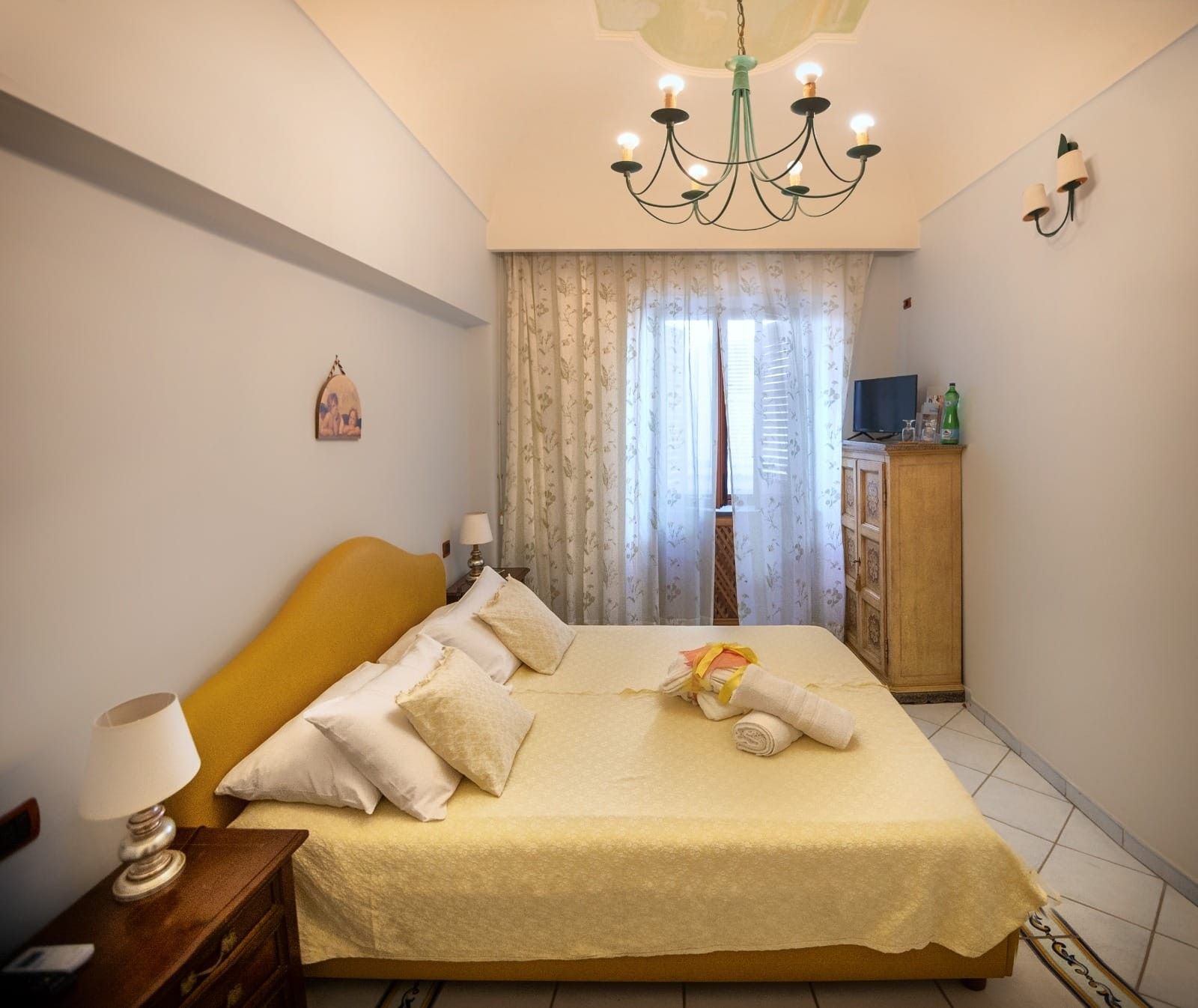 Ein Hotelzimmer mit einem Bett, einem Nachttisch, einer Lampe, einem Fernseher, einem Schrank und einem Fenster mit Vorhängen.
