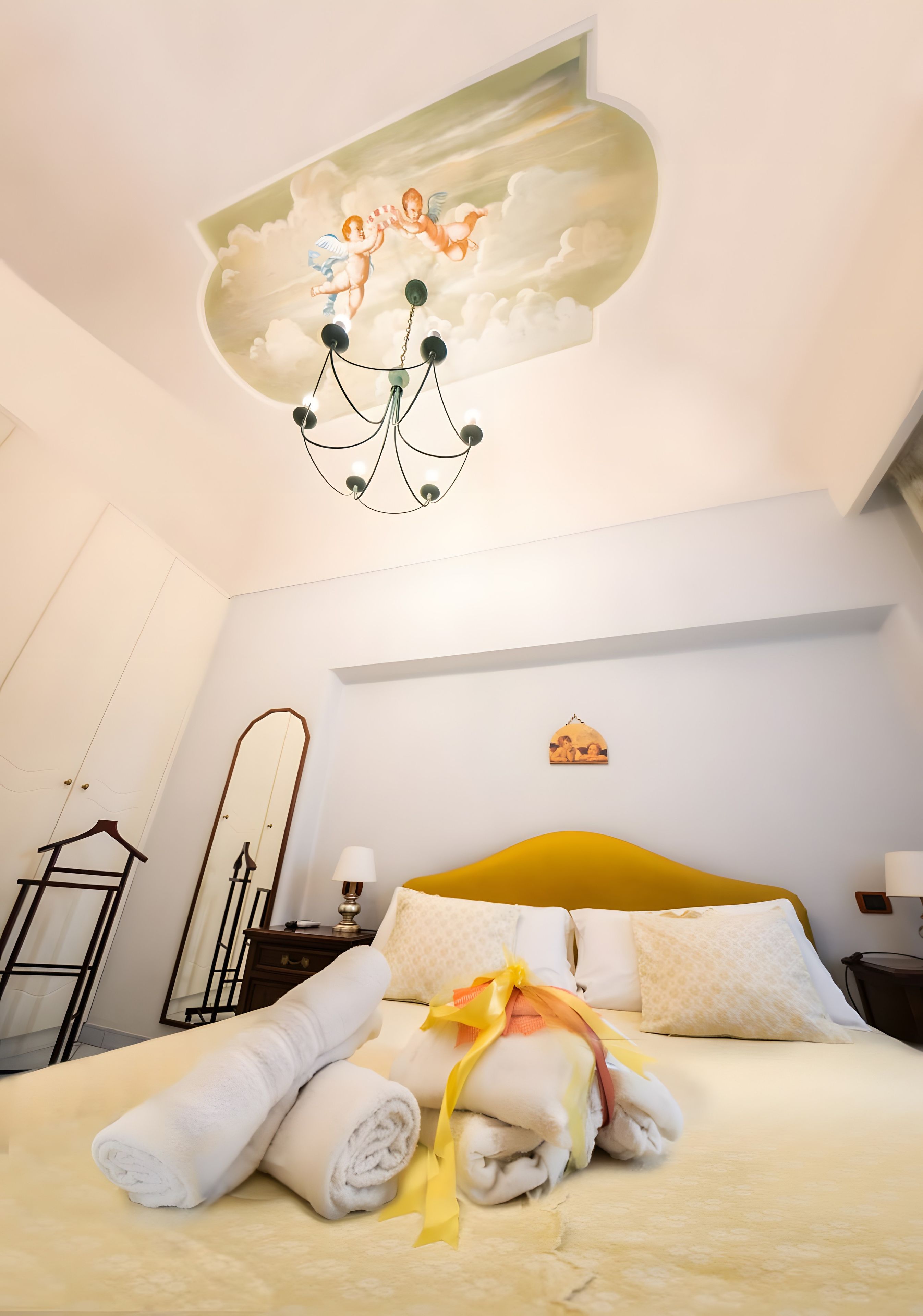 Habitación de hotel con cama, candelabro, espejo y un mural en el techo.