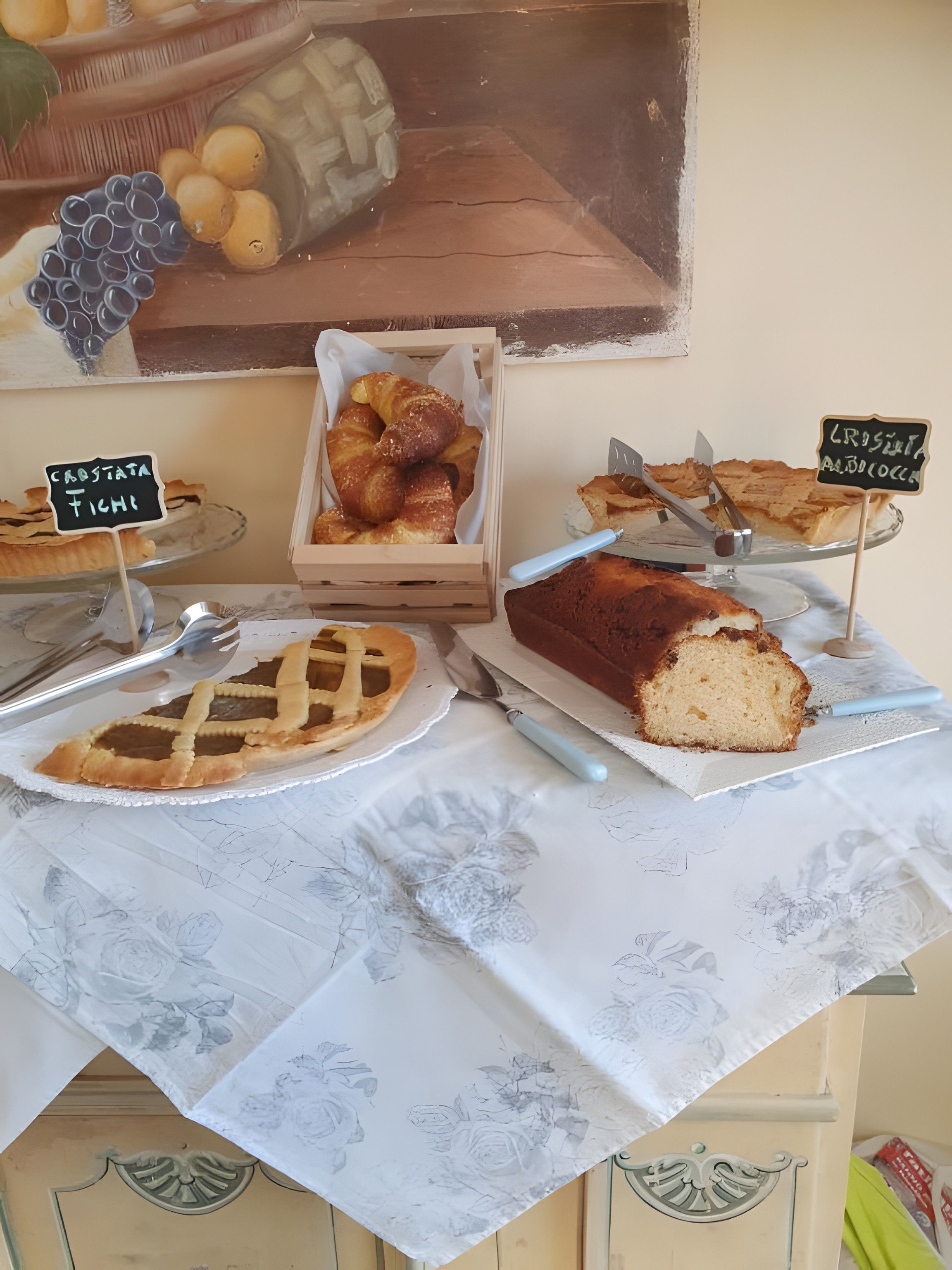 A bakery display with various baked goods, including croissants and a loaf of bread, on a table with a floral tablecloth.