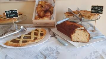 A bakery display with various baked goods, including croissants and a loaf of bread, on a table with a floral tablecloth.