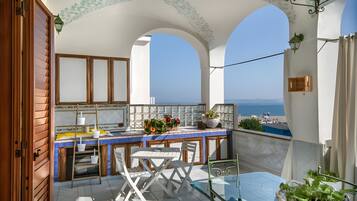 Ein Balkon mit Meerblick, einem Tisch mit Stühlen und einer kleinen Gartenanlage.
