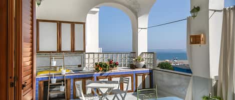A balcony with a view of the sea, a table with chairs, and a small garden area.