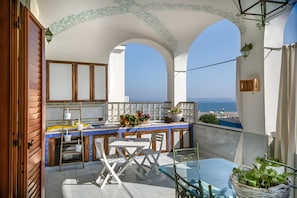 Ein Balkon mit Meerblick, einem Tisch mit Stühlen und einer kleinen Gartenanlage.