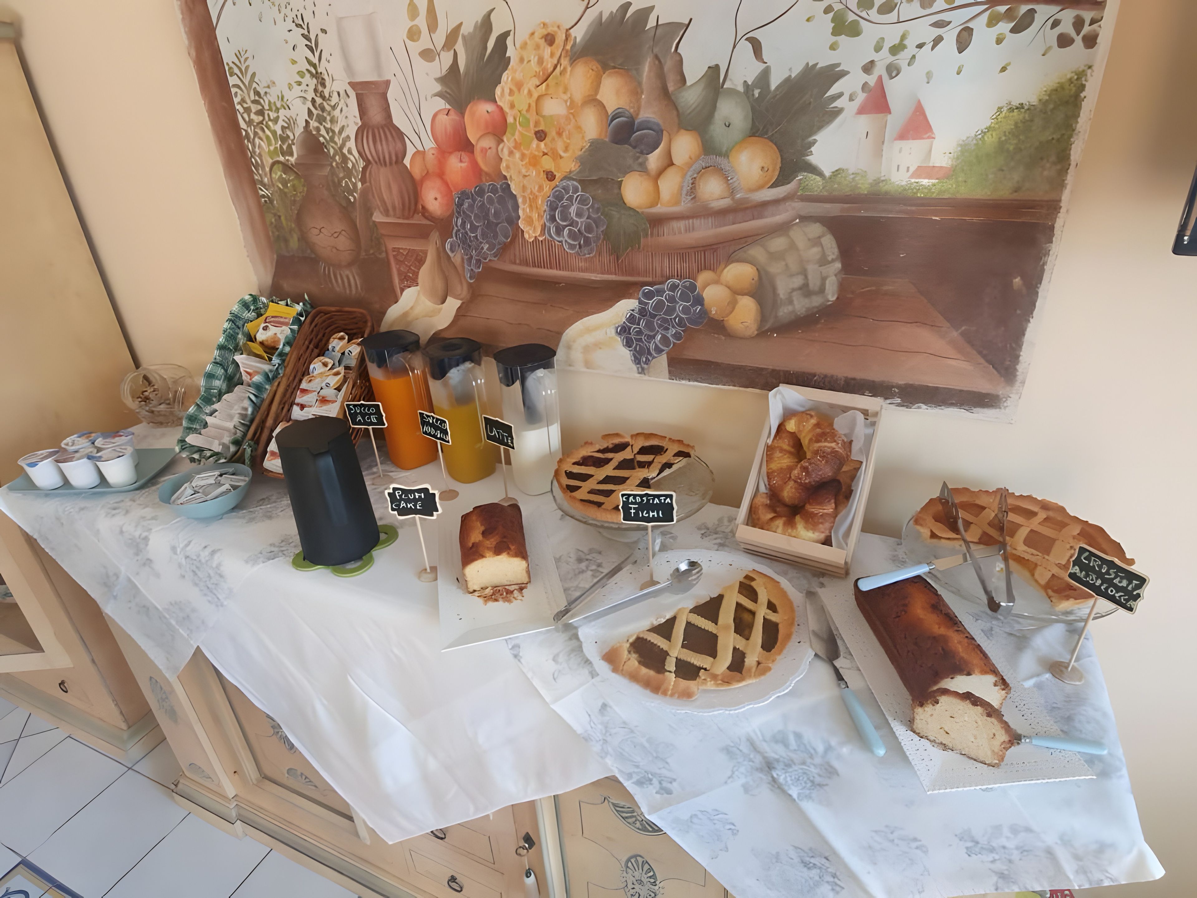 Une table de buffet proposant divers plats et boissons, notamment une tarte, un pain et des récipients étiquetés contenant des jus de fruits.