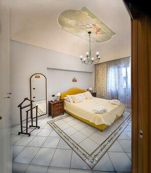 Une chambre d’hôtel avec un grand lit, un lustre, un miroir et un plafond décoratif.