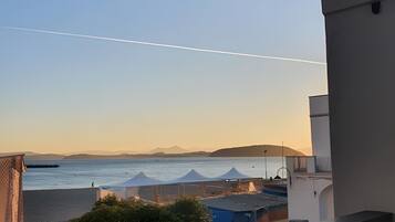 Un balcon avec vue sur la mer, un ciel dégagé et des montagnes à l’horizon.
