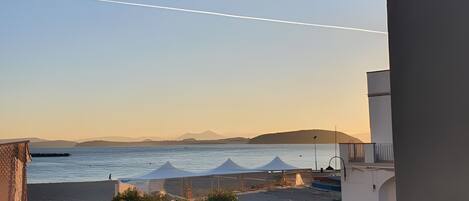 A balcony with a view of the sea, a clear sky, and distant mountains.