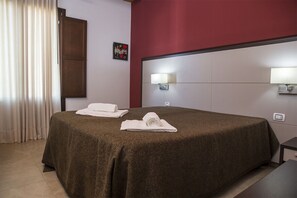 Ett hotellrum med en stor säng, två sänglampor, ett konstverk som hänger på väggen och en dörr.