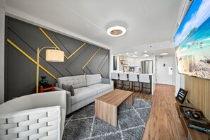 Ett modernt vardagsrum med en grå soffa, ett träbord och en tv-skärm som visar en vacker utsikt.