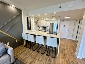 A modern kitchen with a central island, bar stools, and a staircase leading to another level. - Renovated Ocean View 1 Bedroom Apartment @ The Ilikai Waikiki Beach, Honolulu (Honolulu)