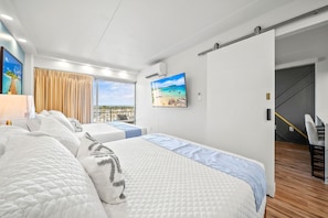Habitación de hotel con dos camas, un ventanal con vistas, un cuadro en la pared y una escalera que lleva a otra zona.