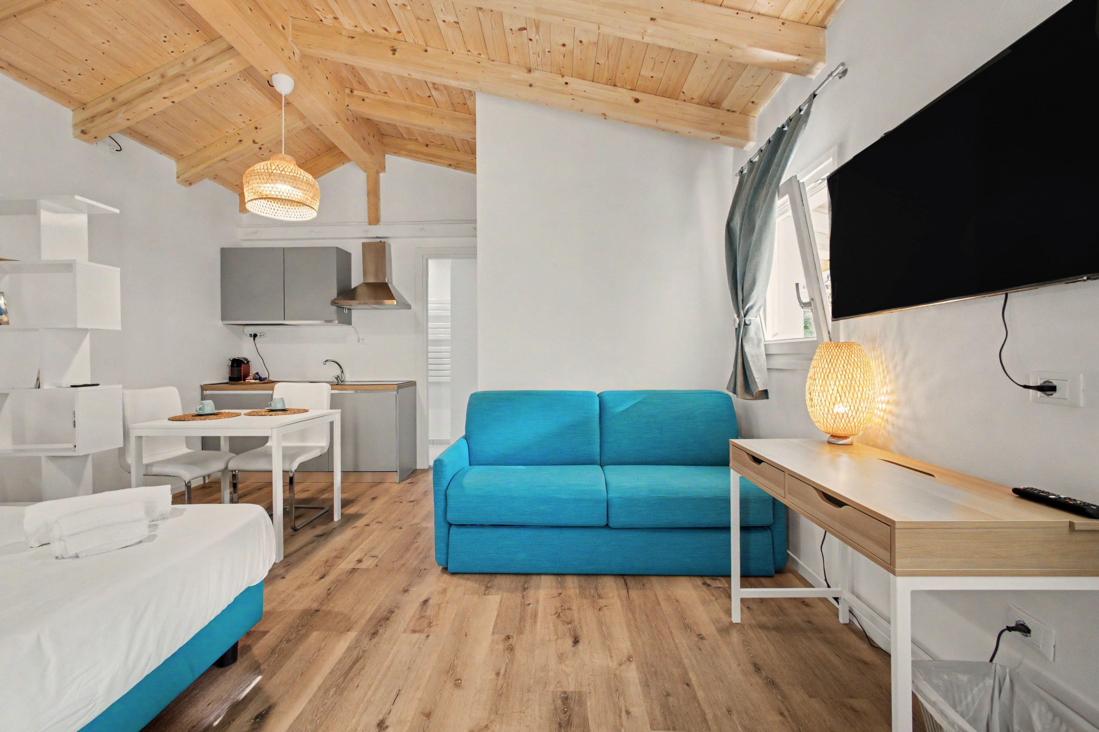 Une pièce moderne et bien éclairée, avec un canapé bleu, une table à manger et un coin cuisine.