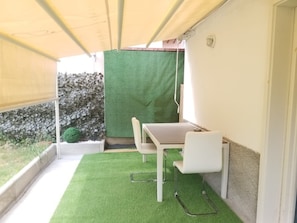 Un piccolo balcone con un tavolo e due sedie, un pavimento di erba sintetica verde e pareti, una bianca e l'altra in pietra, sullo sfondo.