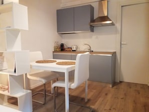 Una cucina compatta con un tavolo bianco, due sedie, un pensile grigio e una cappa in acciaio inossidabile.