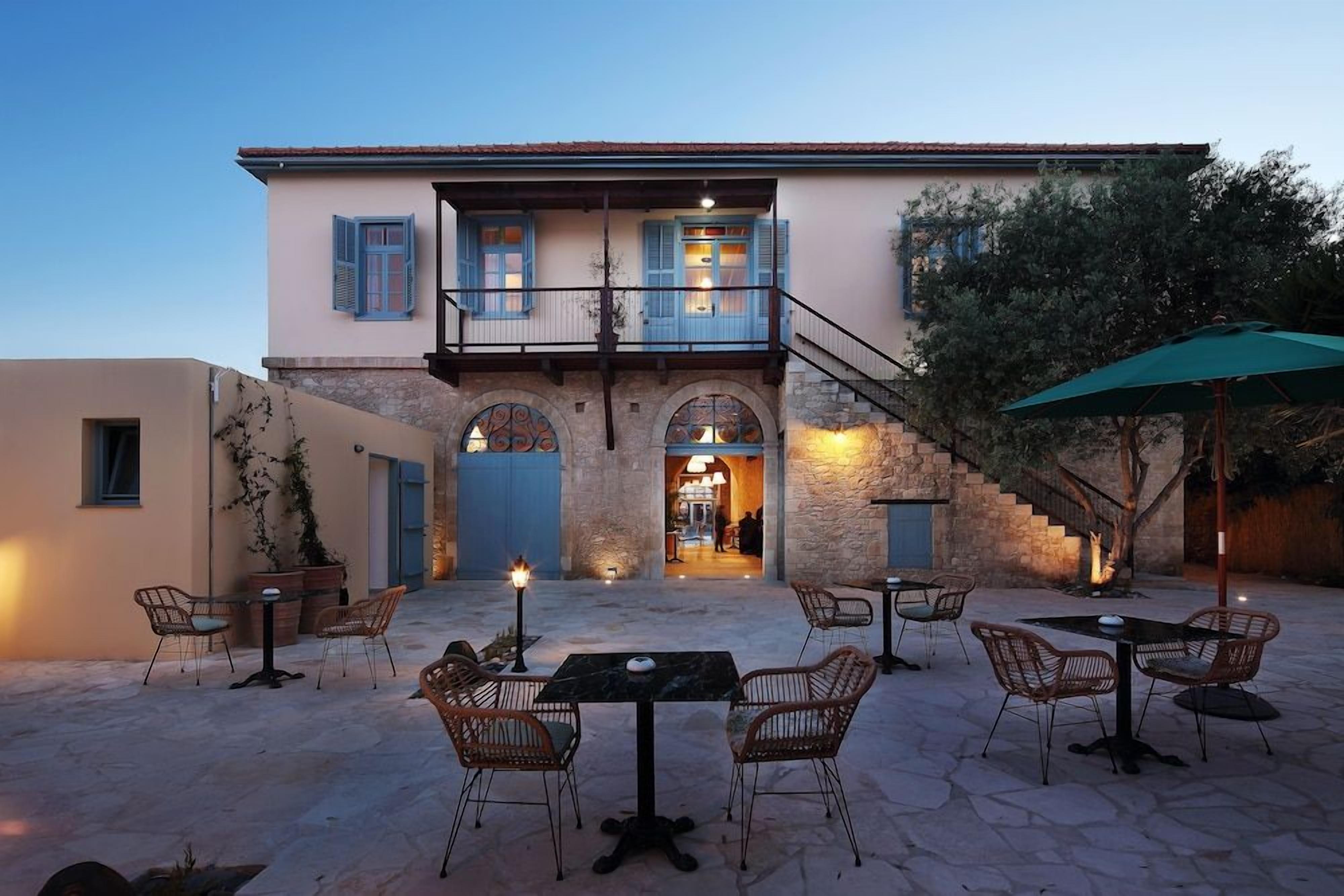 A building with a balcony, outdoor seating area with tables and chairs, and a staircase leading to the entrance.