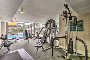 Uma academia com diversos equipamentos de exercício, uma placa indicando o horário de fechamento às 22h e uma piscina visível pelas janelas.