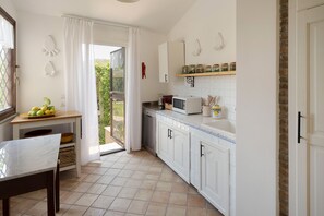 Eine Küche mit Esstisch, Kühlschrank, Mikrowelle und einem Fenster mit Vorhängen.
