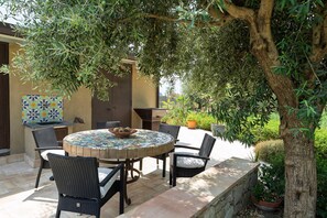 Patio esterno con tavolo rotondo, quattro sedie e tovaglia con decorazioni a mosaico.