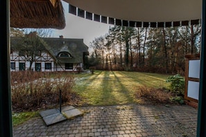 Ein Innenhof mit einem reetgedeckten Gebäude, einer gepflasterten Fläche und Blick auf ein traditionelles Gebäude mit Schrägdach.