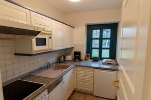 Eine kompakte Küche mit weißen Schränken, einer Mikrowelle, einer Kaffeemaschine und einem Fenster mit Blick auf Bäume.