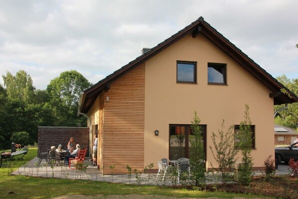 A two-story building with a sloped roof and a beige exterior. There are outdoor seating areas with tables and chairs. - Vrbo Property (Lenz)