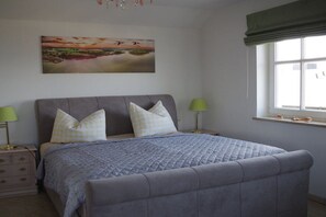 Un dormitorio con cama, dos mesitas de noche, una ventana con vistas y un cuadro en la pared.