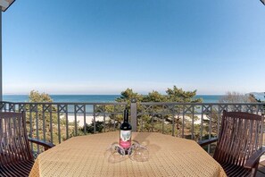 Une terrasse avec une table et des chaises, donnant sur une plage et la mer.
