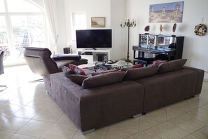 A living room with a brown sofa, a flat-screen TV, a coffee table, and a dining area with chairs. - Apartment with 2 bedrooms (Ostseebad Binz)