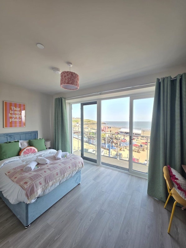 A bedroom with a large bed, a view of the beach, and a balcony with a chair. - Elysium Beachfront Apartment | Sea Views & Parking (Barry)